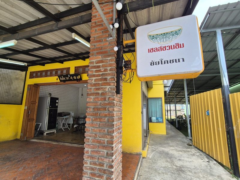 ป้ายเชลล์ชวนชิม ชัยโภชนา แขวนที่เสาอิฐข้างหน้าร้านสีเหลือง