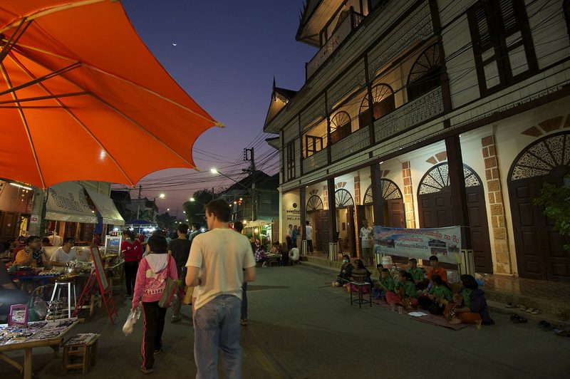 ถนนคนเดินหน้าเรือนไม้เก่าสองชั้น มีร่มสีส้มและแผงของขายริมทาง